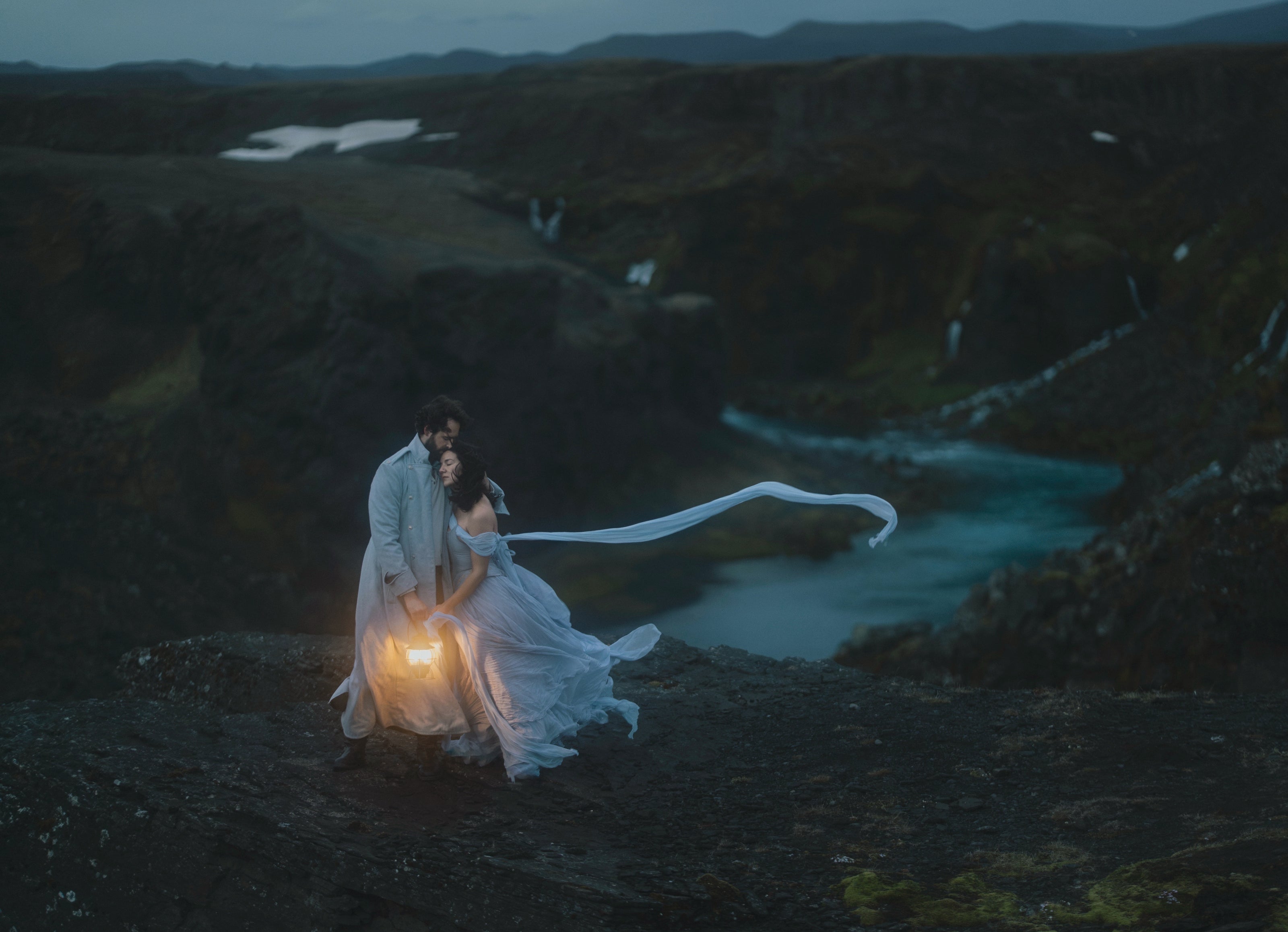A wedding couple stand with a glowing lantern amongst a backdrop of waterfalls and a glacial blue river in Iceland