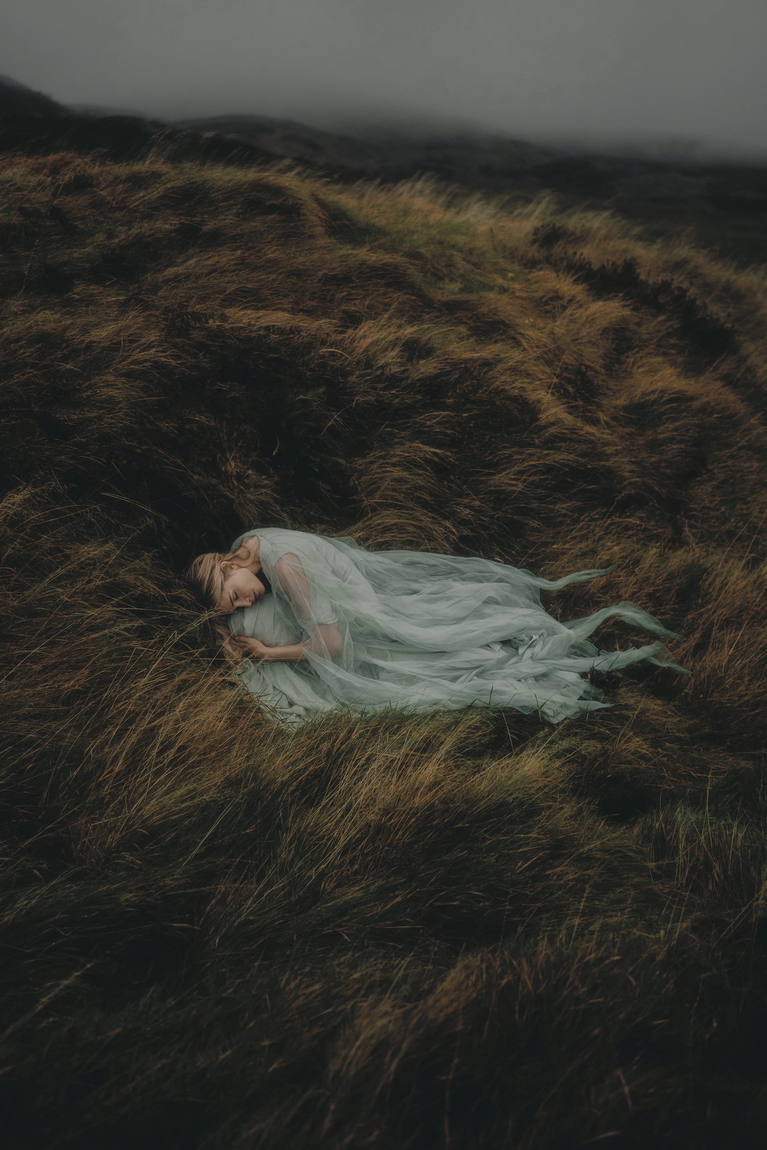 Woman in a green dress lying on a grassy field with a dark, moody atmosphere