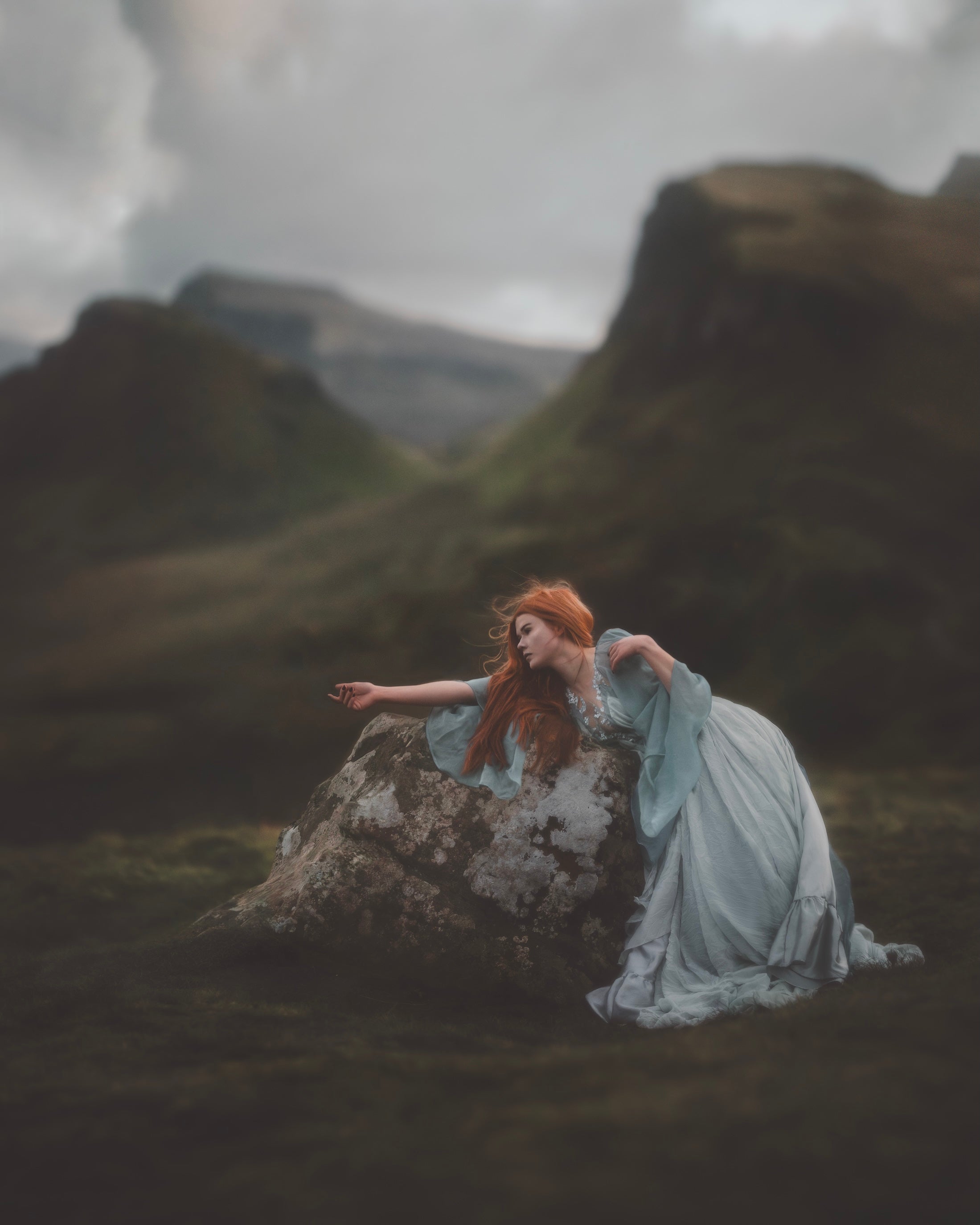 PreRaphaelite redhead in blue dress on a rock in Scotland