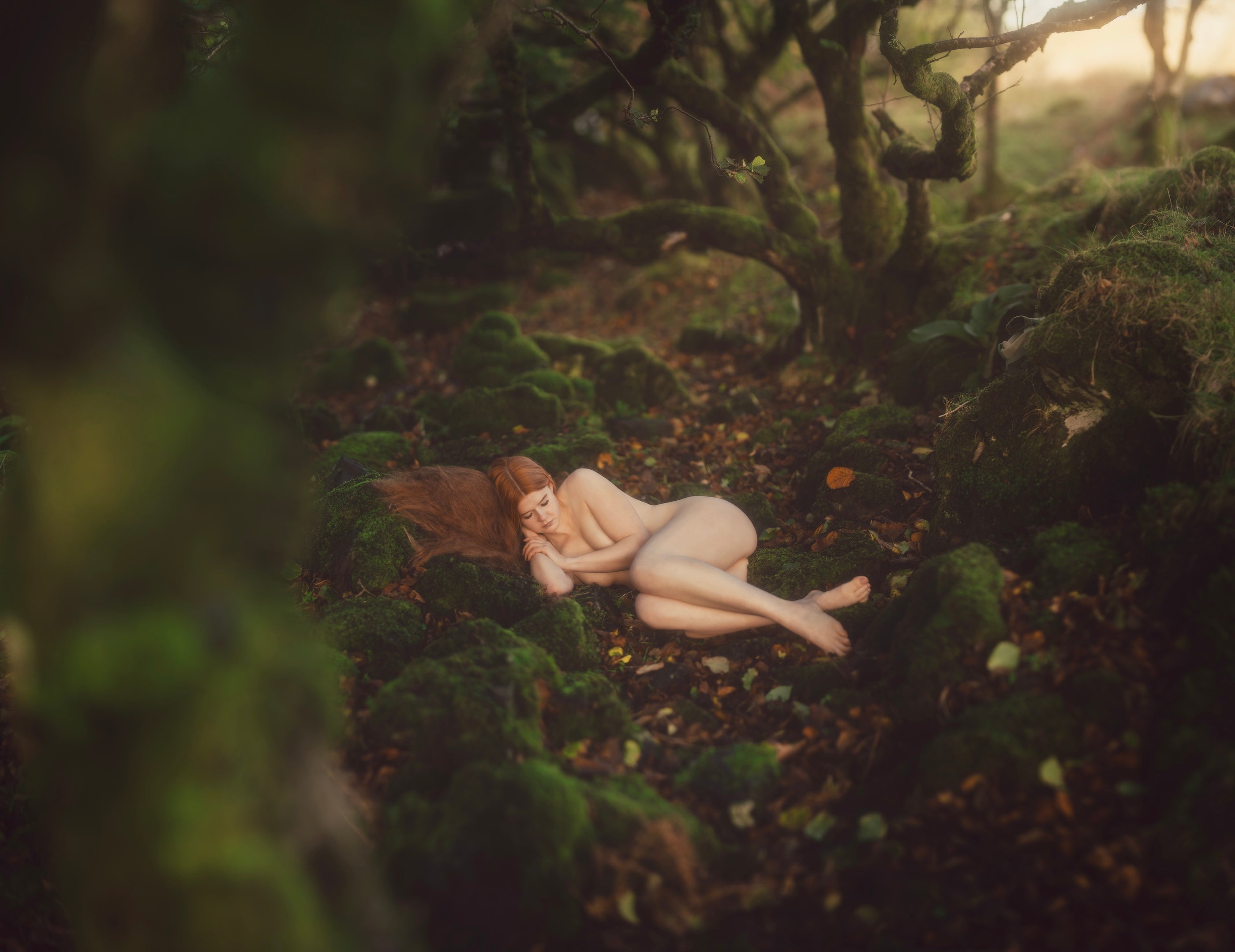 Redhead fairy lying on a mossy forest floor surrounded by twisted trees