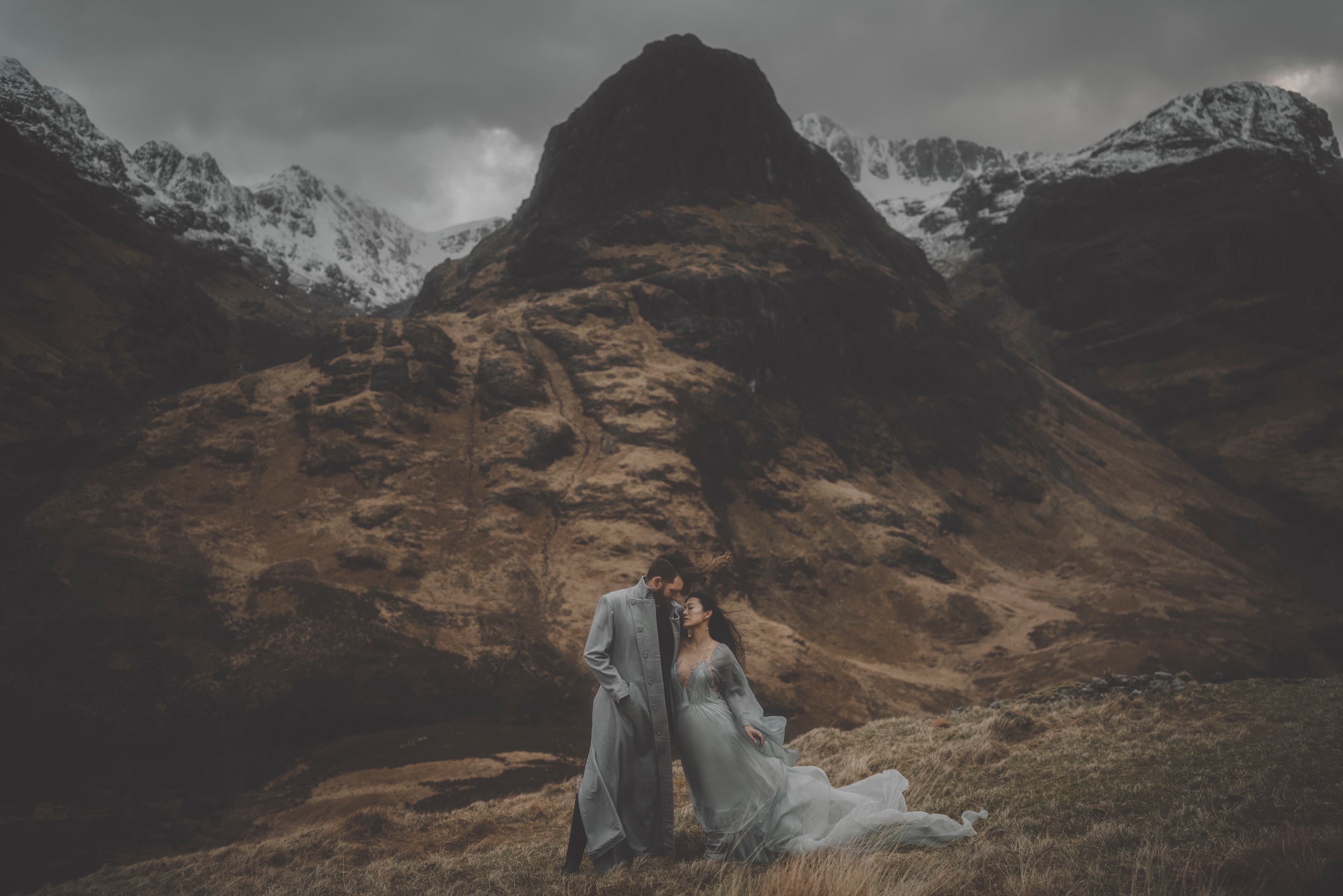 Winter Elopement in Scotland: A couple in wedding attire standing in a mountainous landscape with snow-capped peaks.